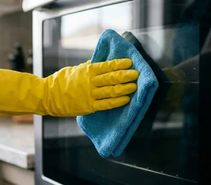 Cleaner wiping the glass door of a stainless steel oven