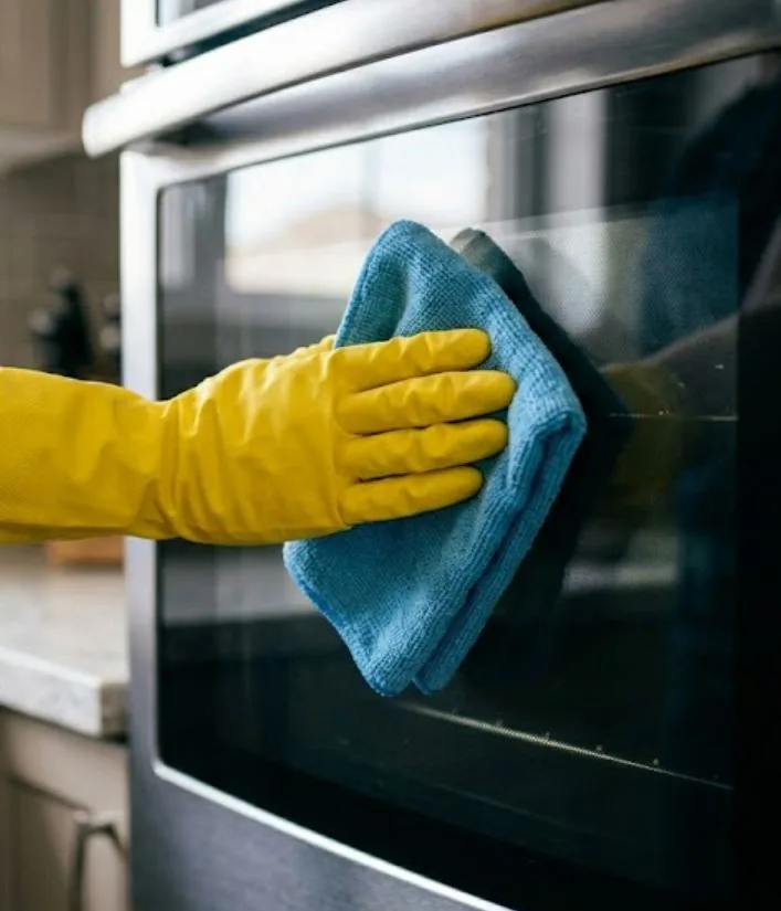 Cleaner wiping the glass door of a stainless steel oven
