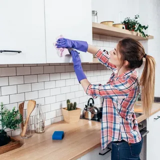 Cleaner wiping kitchen wall tiles beside small appliances
